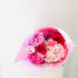 Bouquet de flores rosadas, agrupadas por tonalidades, envuelto en papel de seda rosado claro y fotografiado en un pedestal blanco
